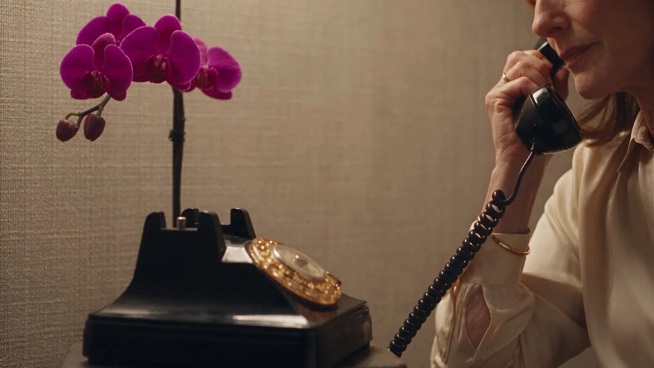 Eine Hand nimmt den Hörer eines schwarzen Telefons ab, daneben eine Orchidee